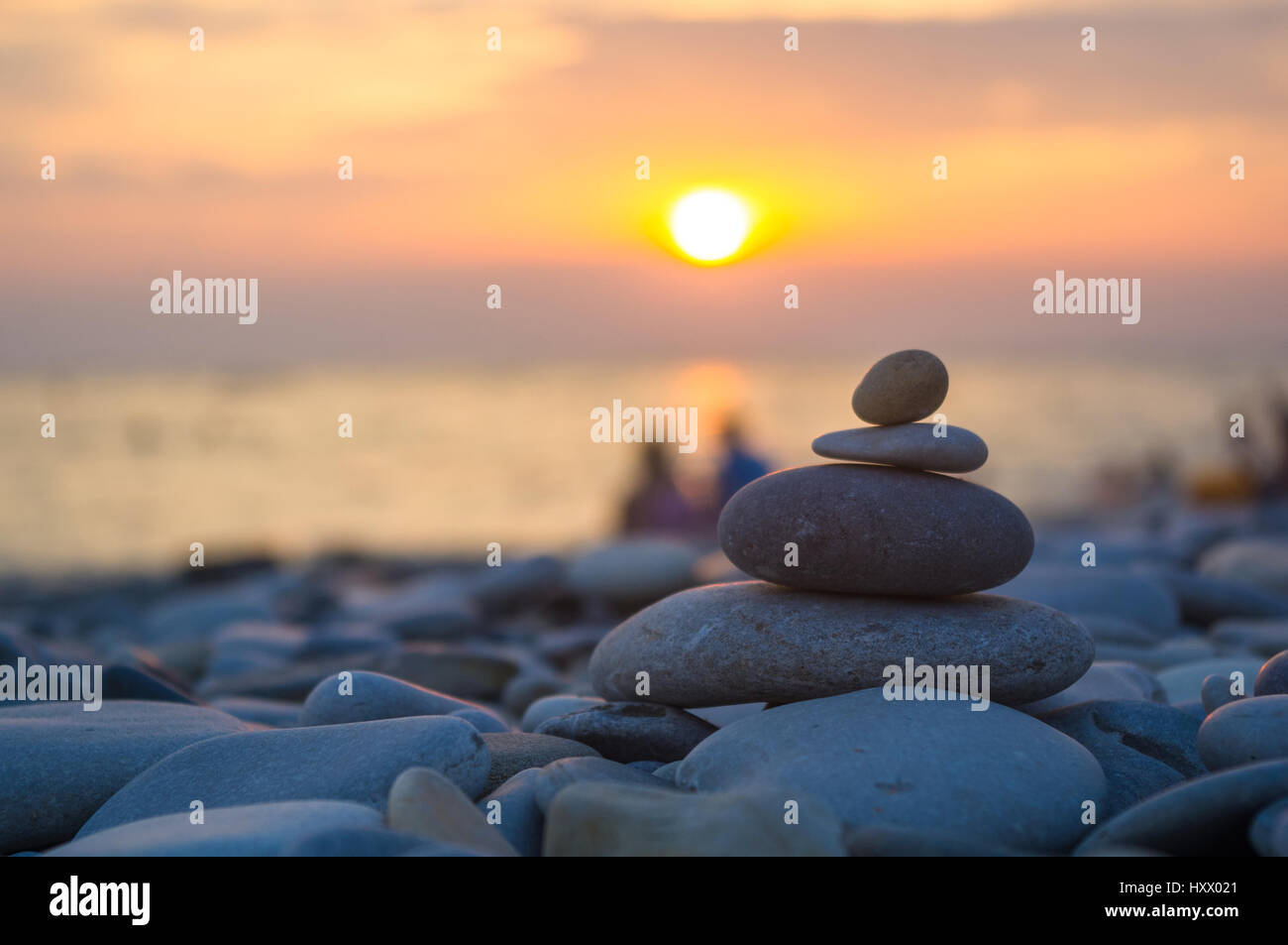 Un giovane e ripiegati a piramide Zen pietre ghiaia sul mare spiaggia al tramonto Foto Stock