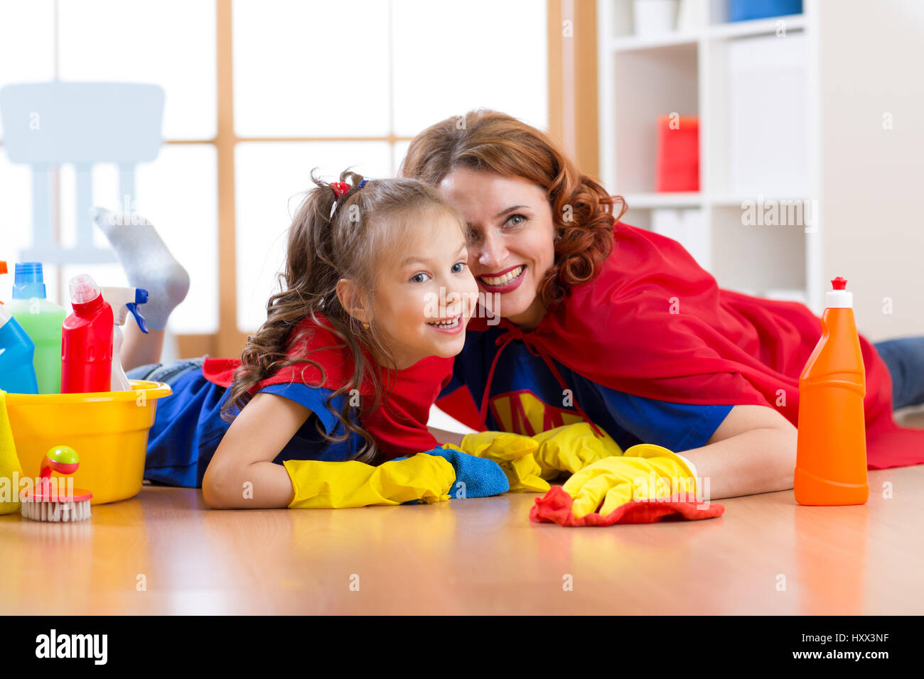 Carino madre e suo figlio figlia vestiti come supereroi la pulizia del pavimento e sorridente Foto Stock