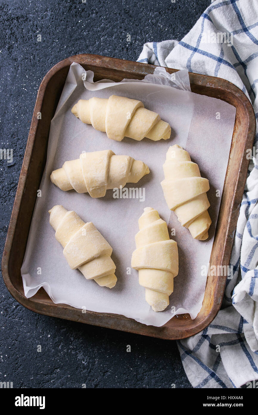 Materie crudi croissant sulla carta da forno nel vecchio forno il vassoio con carta asciugatutto per black texture di sfondo di calcestruzzo. Vista superiore Foto Stock
