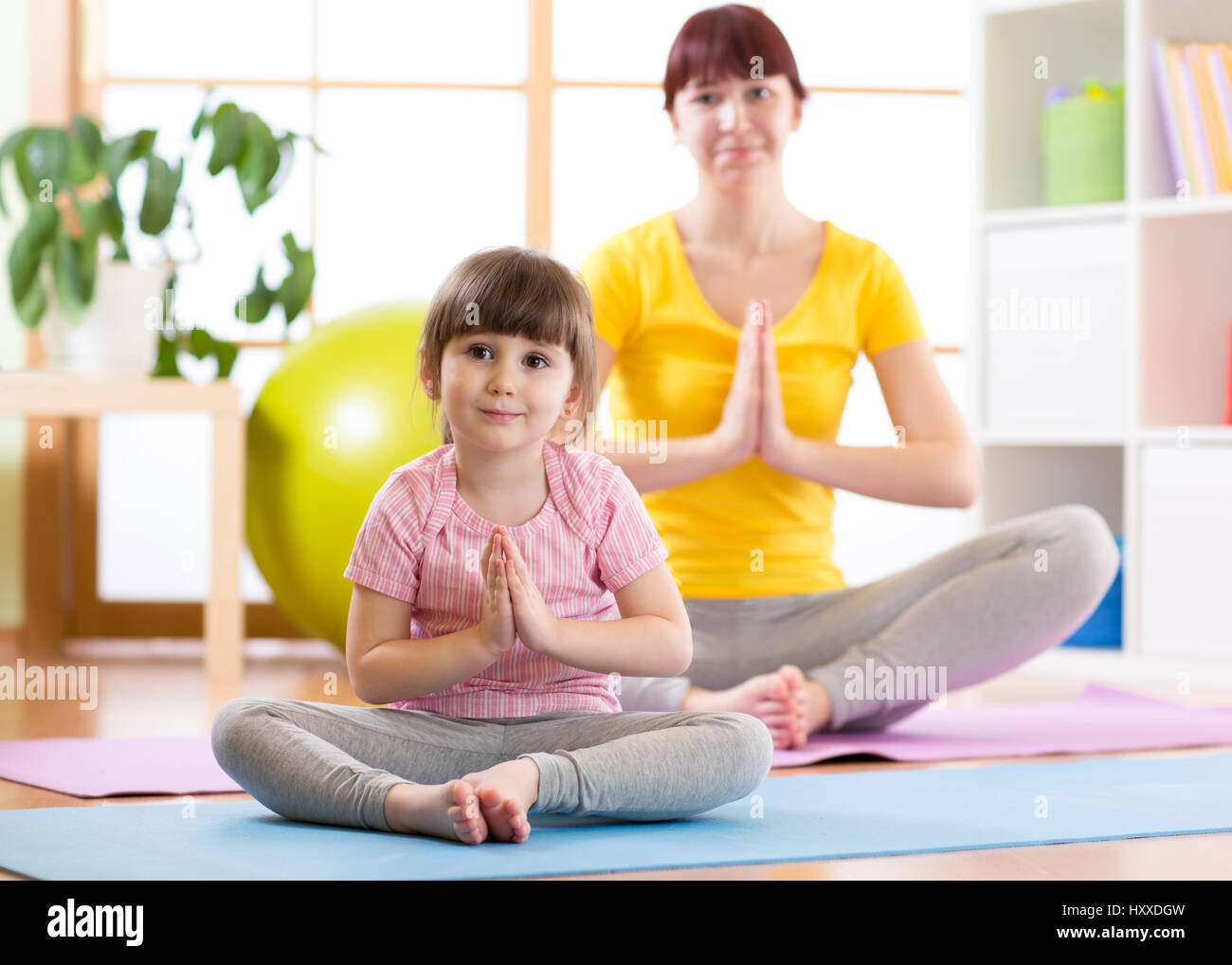 Giovane donna e la figlia facendo esercizi yoga a casa Foto Stock