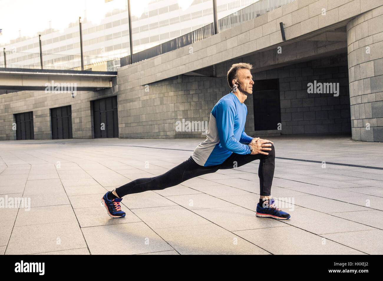 Bello atleta uomo in nero blu sport stiramento uniforme corpo, in fase di riscaldamento e si è pronti per fare jogging. Foto Stock