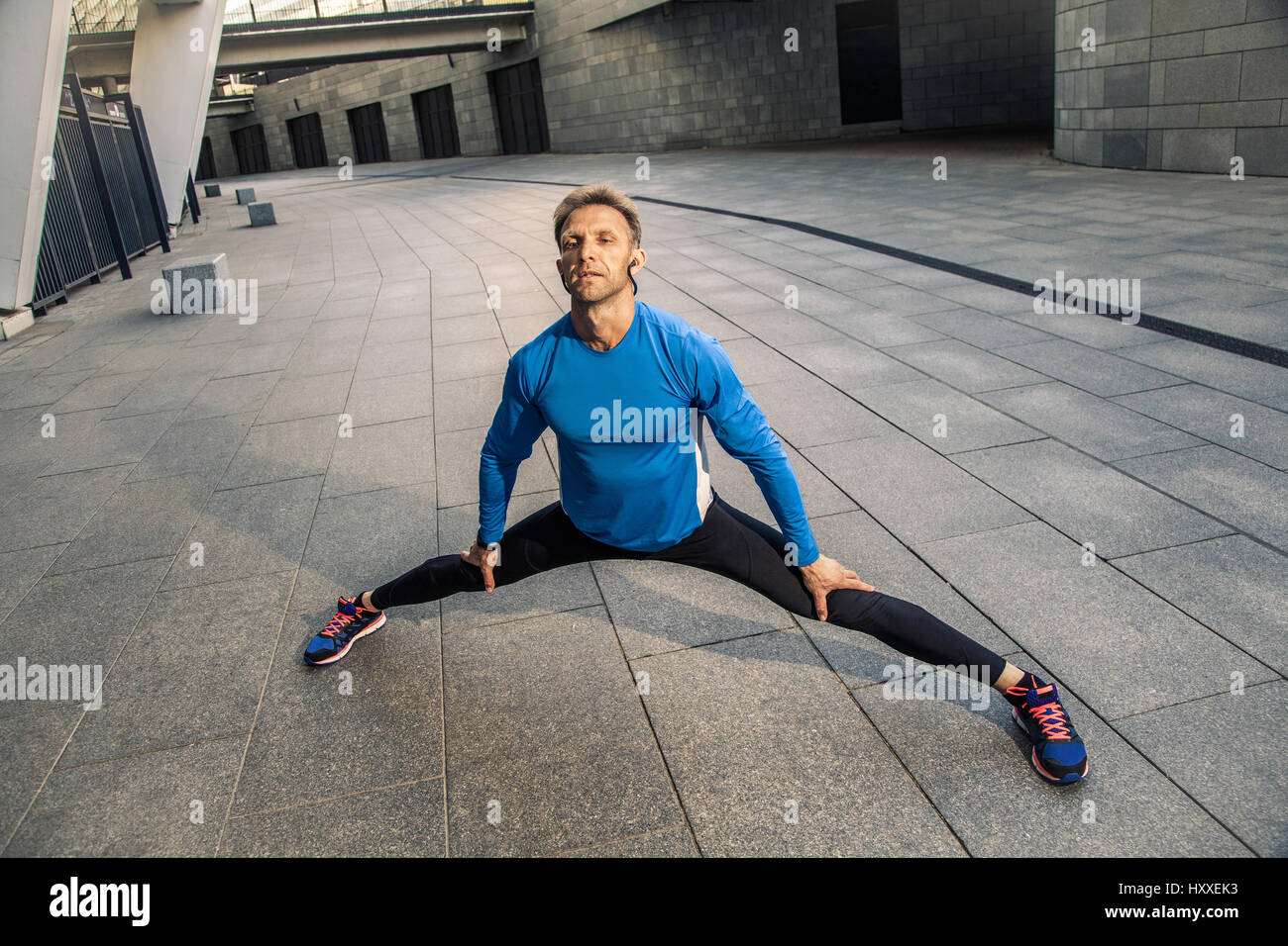 Bello atleta uomo in nero blu sport stiramento uniforme corpo, in fase di riscaldamento e si è pronti per fare jogging. Foto Stock