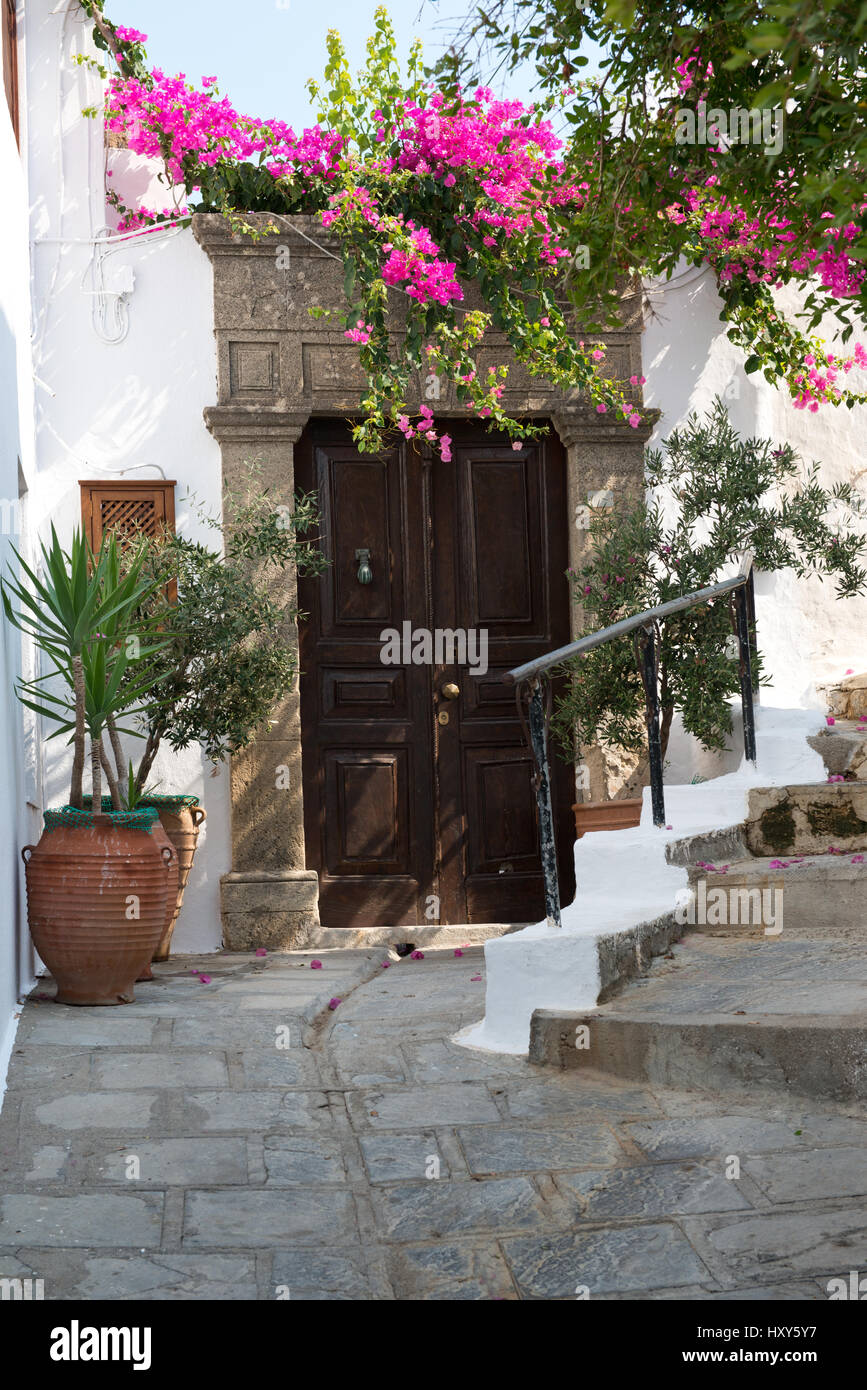 Portale di antica casa con porta di legno, cornice in pietra,bouganville e vasi di ceramica nel villaggio di Lindos, Rodi, Grecia Foto Stock