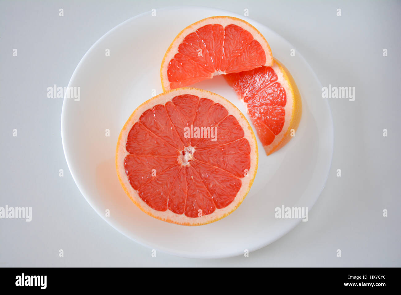 Angolo di alta vista di un primo piano di pompelmo rosa a metà e le fette su una piastra bianca e sfondo Foto Stock