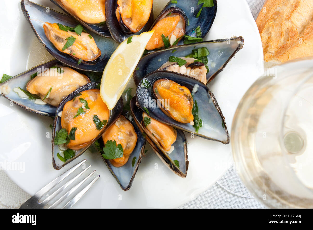 Le cozze con vino bianco e salsa a base di prezzemolo con un bicchiere di vino bianco e pane Foto Stock