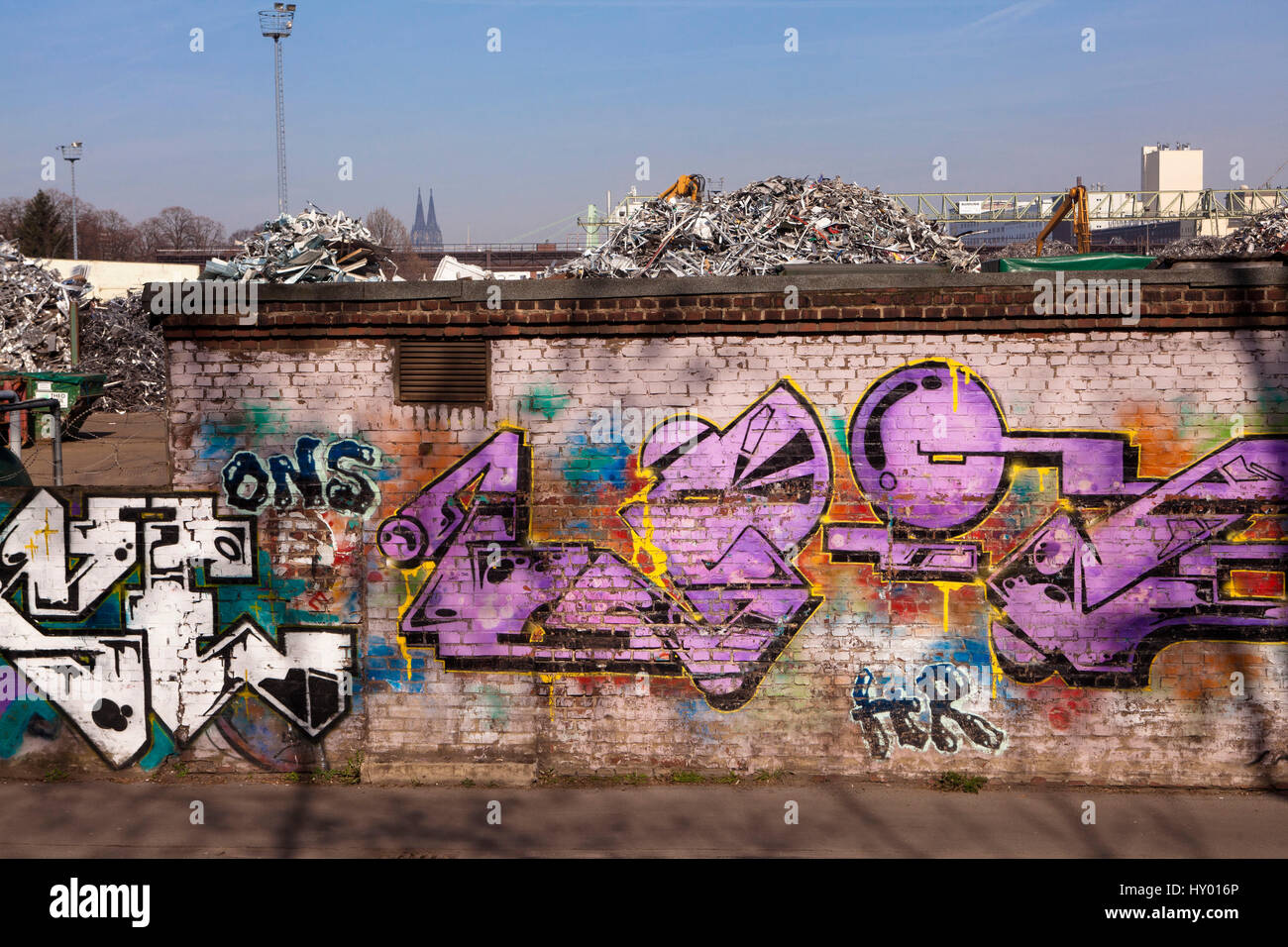 Germania, Colonia, rottami di cantiere con il vecchio metallo nel quartiere Deutz, sullo sfondo la cattedrale, a parete con graffiti. Foto Stock