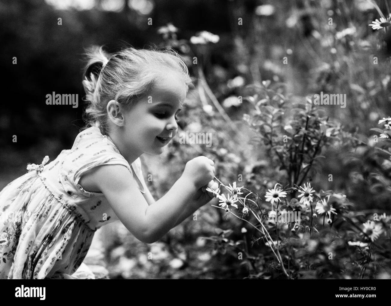 Giovane ragazza bionda a caccia di fiori nel giardino Foto Stock
