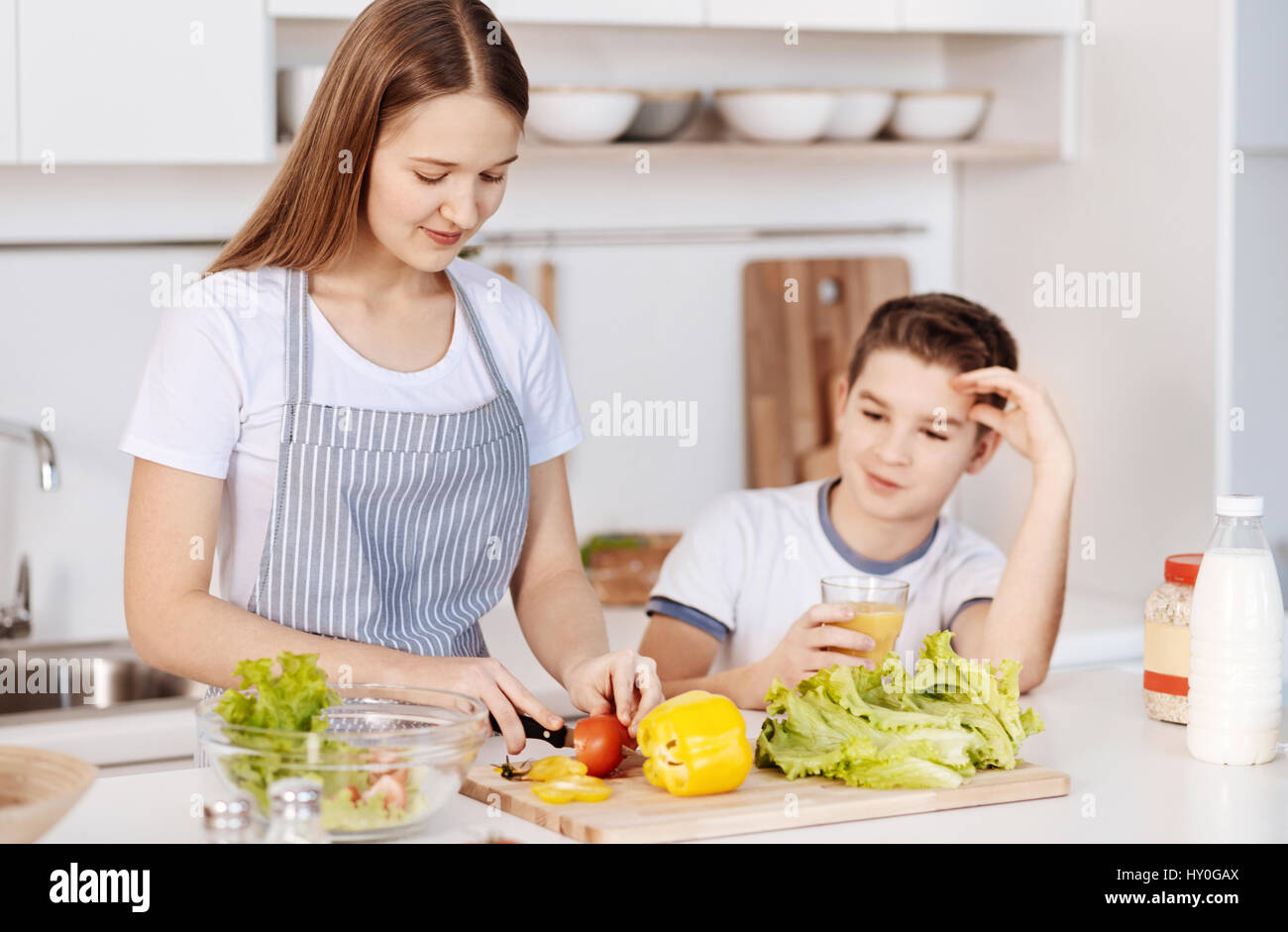 Mangiare sano. Positivo teanage piacere ragazza il taglio di verdure e insalate preparazione permanente, mentre in cucina con il suo fratello più giovane Foto Stock