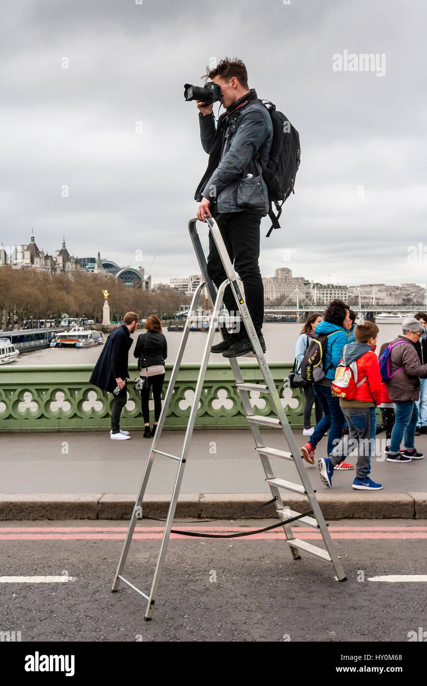 Un fotografo sorge su una scala a pioli per scattare fotografie di persone sul Westminster Bridge una settimana dopo l'attacco terroristico, London, Regno Unito Foto Stock