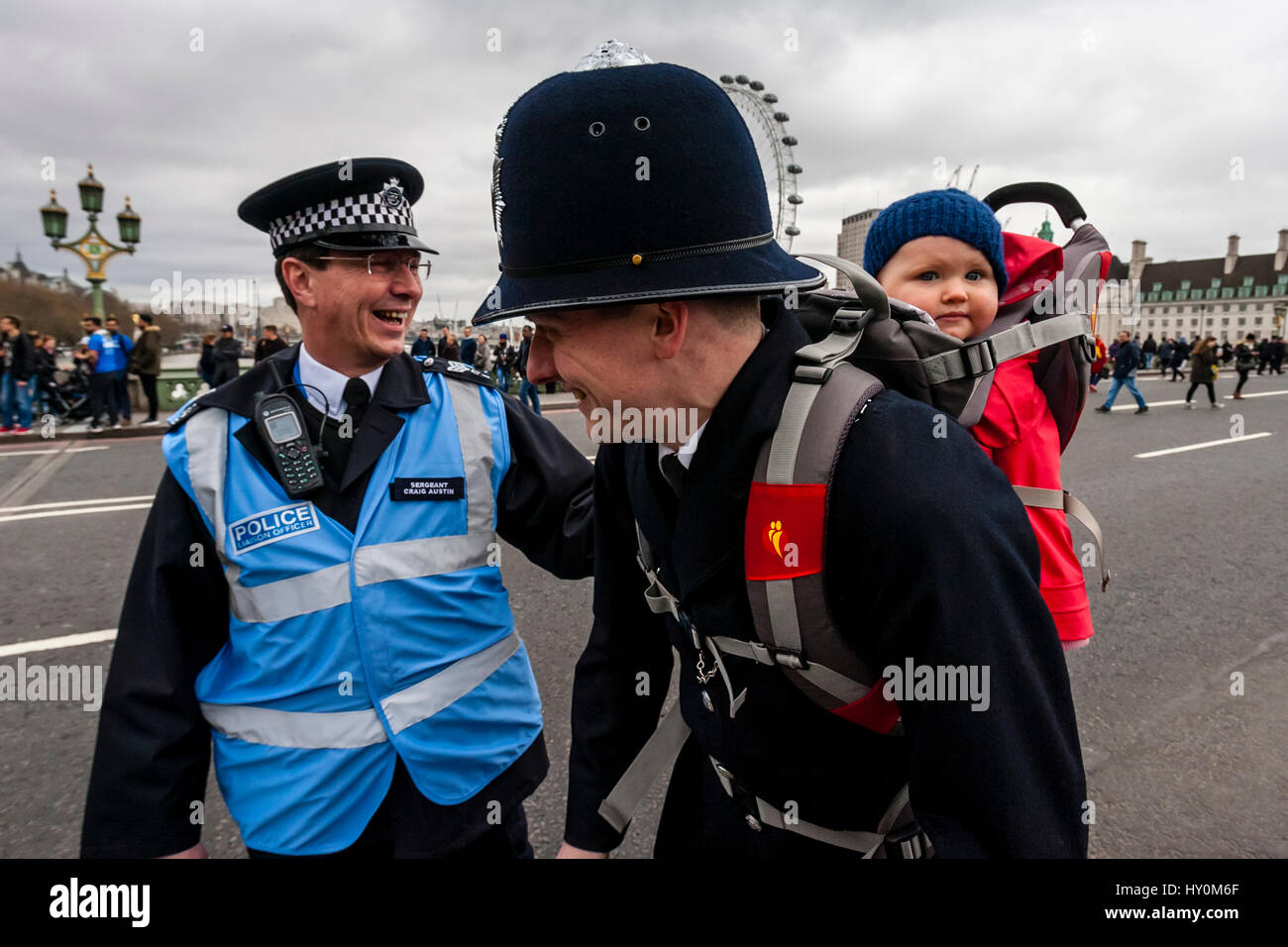 Un poliziotto maschio che porta un bambino in un bambino portatore, Westminster Bridge, London, Regno Unito Foto Stock