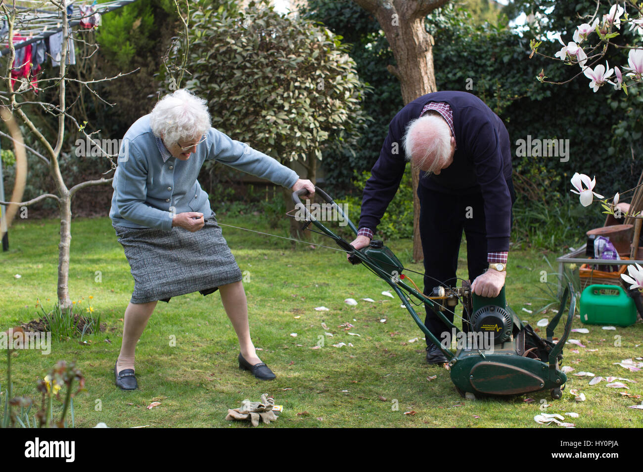 I pensionati anziani cercando di avviare una benzina tosaerba in un inglese giardino residenziale su una molla pomeriggio, Surrey, England, Regno Unito Foto Stock