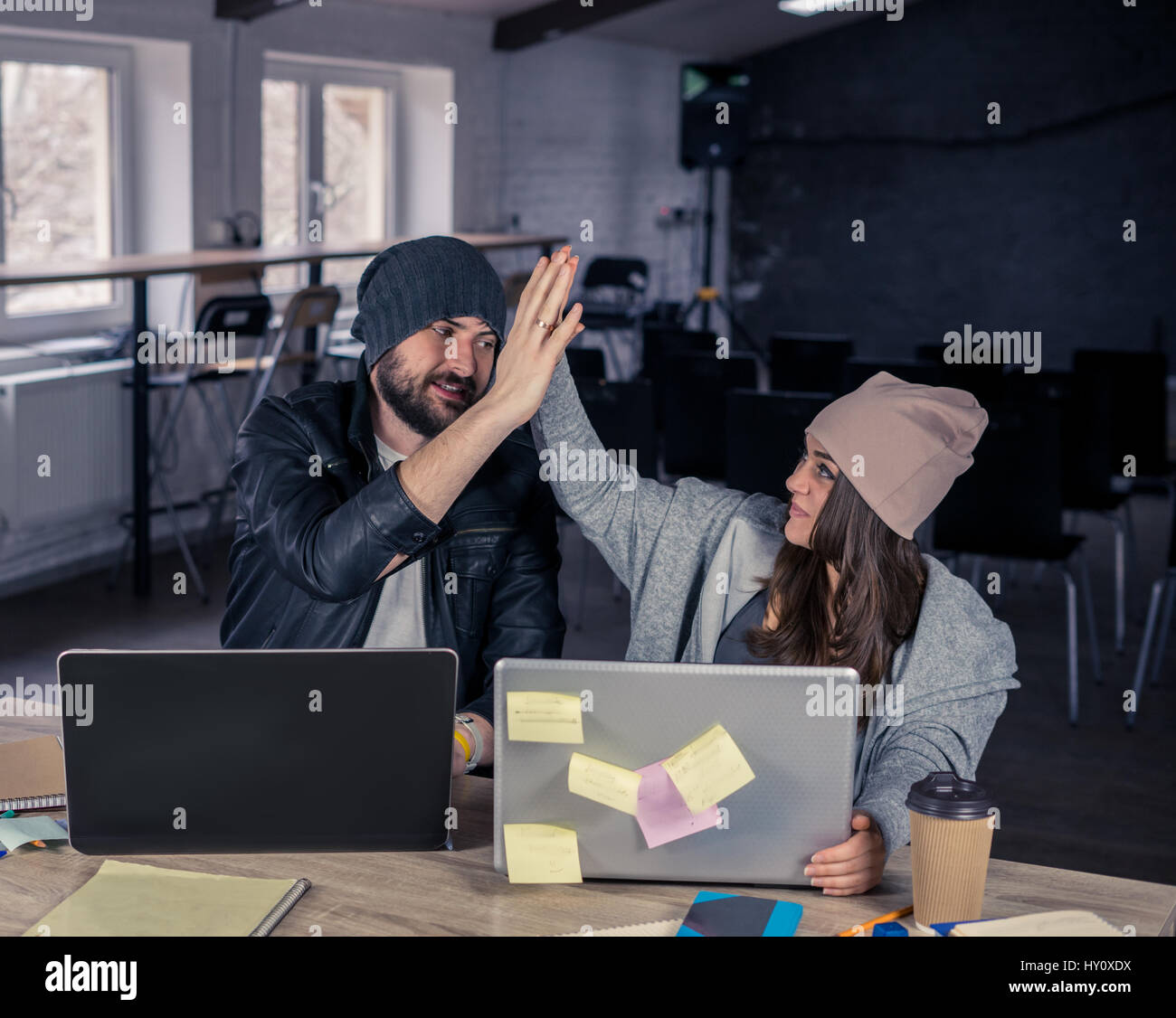 Sorridente studente moderno giovane utilizzando computer portatili e dando alta cinque in ufficio o sala. Foto Stock