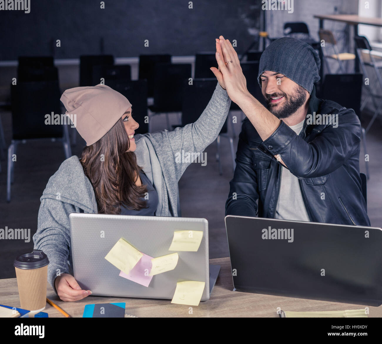 Sorridente hipster degli studenti che utilizzano computer portatili e dando alta cinque in ufficio o sala. Foto Stock