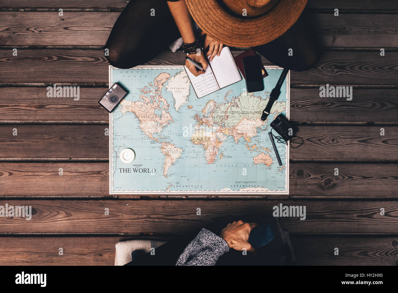 Uomo e donna vacanza di pianificazione utilizzando una mappa del mondo e altri accessori da viaggio. Donna rilevando i punti della discussione in un piccolo diario. Foto Stock