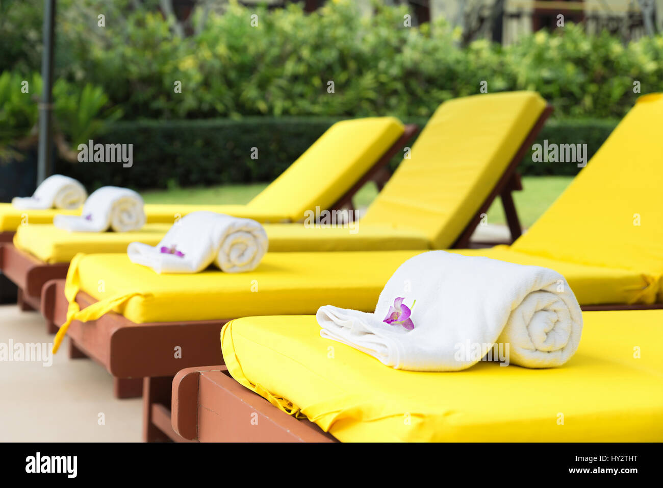 Arrotolato asciugamani sui lettini giallo in piscina al resort. Foto Stock