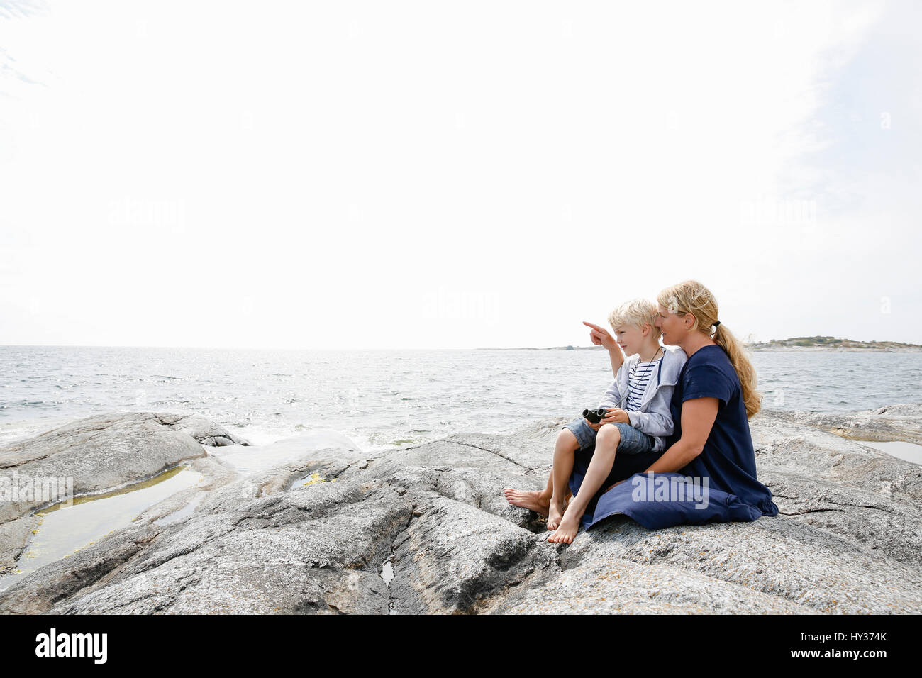 La Svezia, arcipelago di Stoccolma, Sodermanland, Huvudskar, madre e figlio (6-7) seduto sul litorale roccioso Foto Stock
