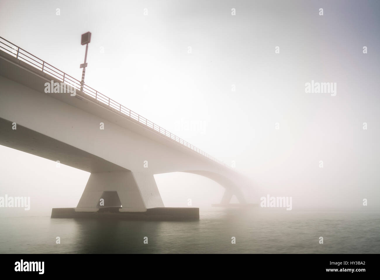 Zeeland ponte (Zeelandbrug) coperta di nebbia durante il sorgere del sole in inverno. Bassa visibilità rendendo il sole che splende attraverso la nebbia la Zeeland bridge è amore Foto Stock