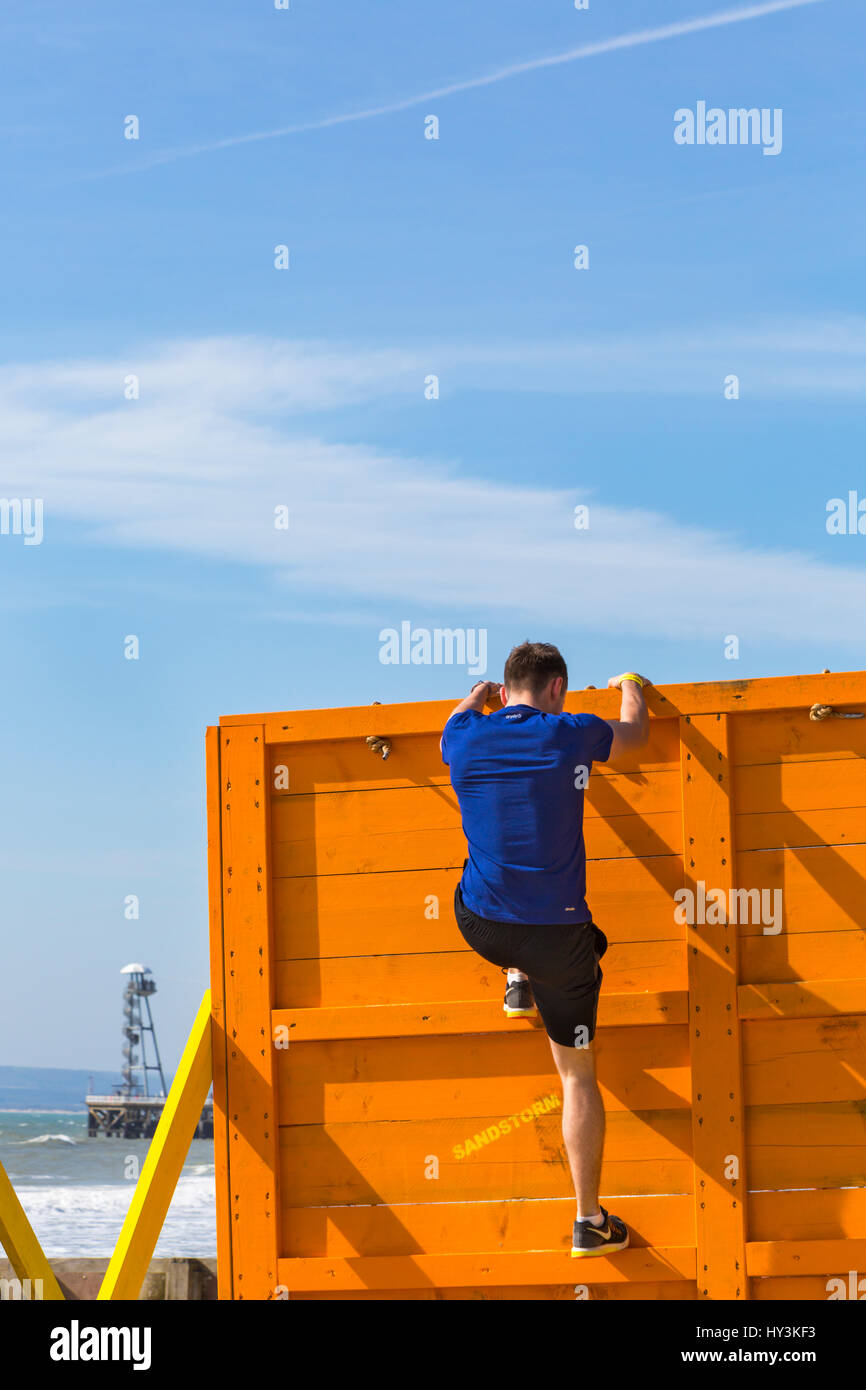 Scavalcando il cliffhanger ostacolo, parte della tempesta di sabbia spiaggia sfida, sul Bournemouth Beach, un Beach Assault Course in Marzo Foto Stock