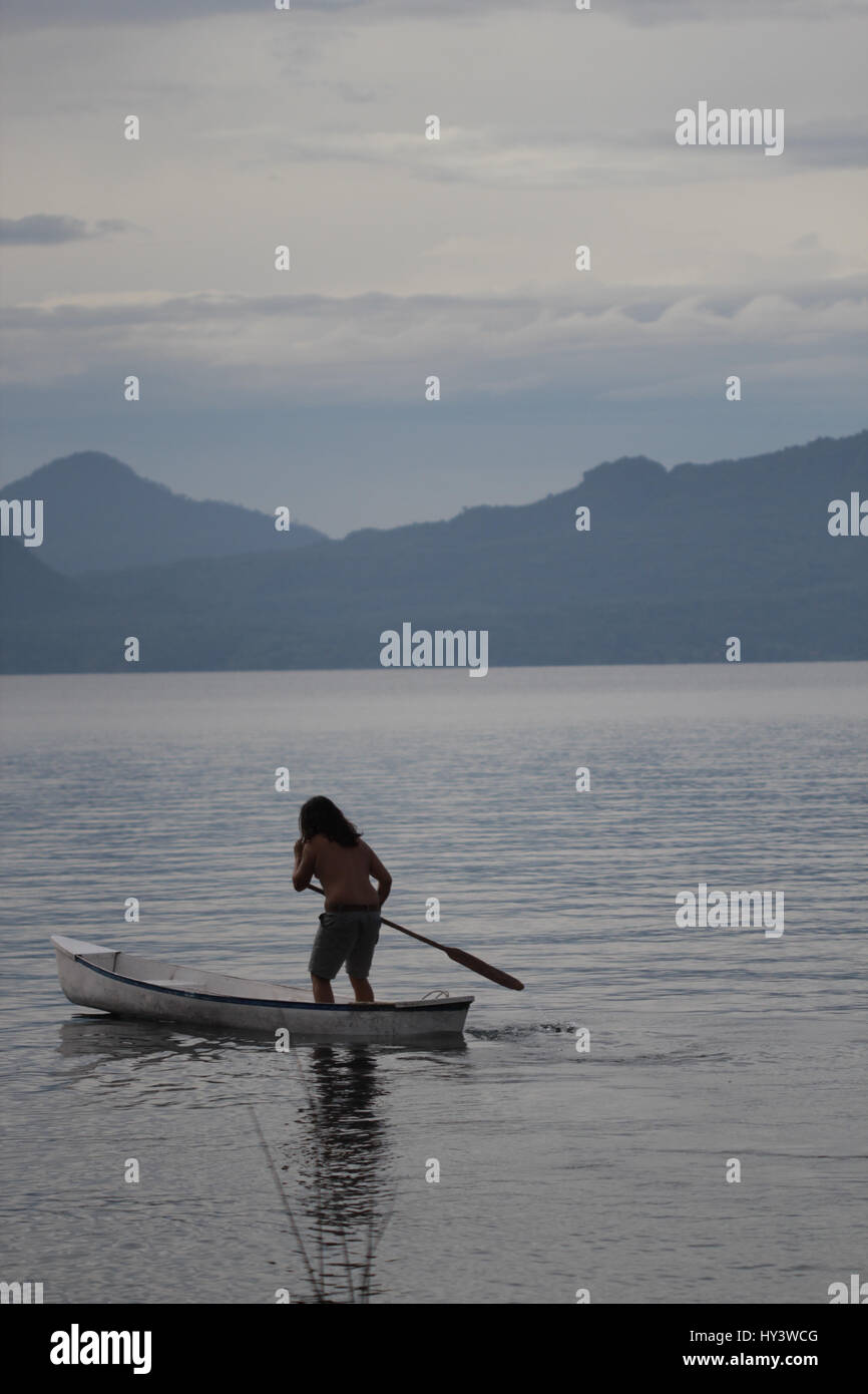 Locali di persona di sesso maschile in Guatemala in piedi nella sua barca e nuoto verso l'altro lato del lago Foto Stock