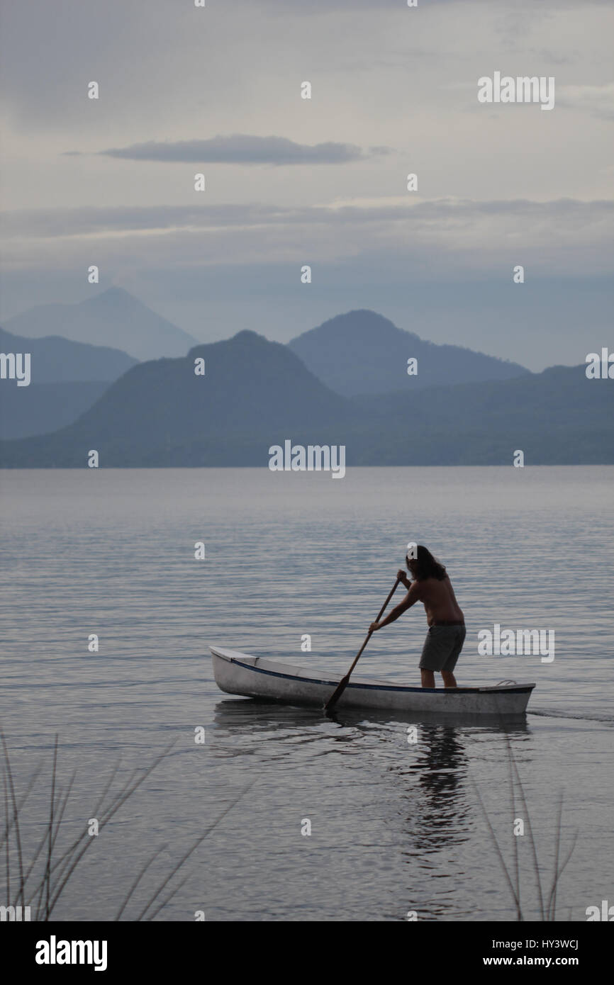 Locali di persona di sesso maschile in Guatemala in piedi nella sua barca e nuoto verso l'altro lato del lago Foto Stock