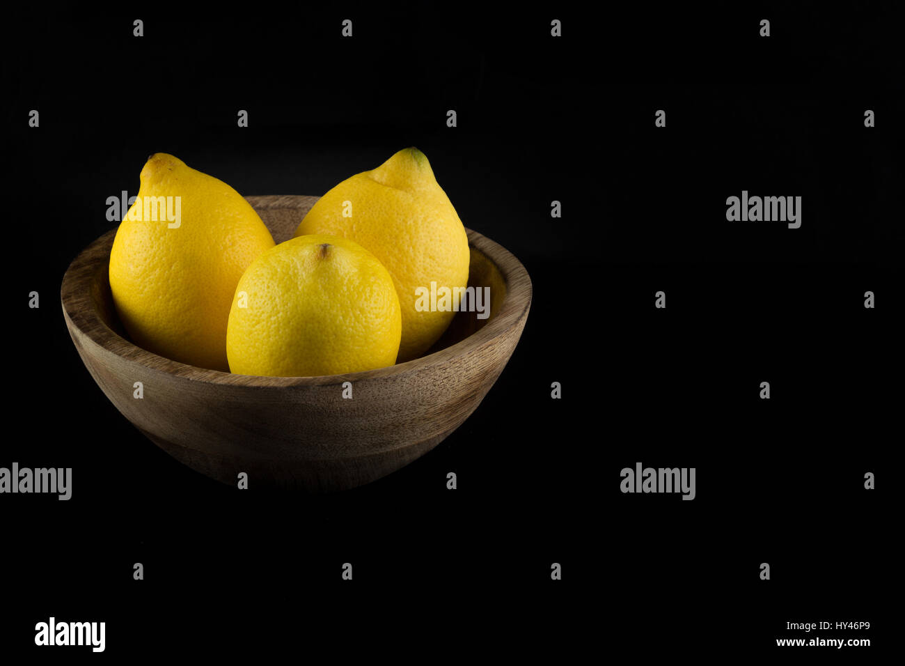 I limoni in una naturale fatta a mano in vero legno ciotola isolato in sfondo nero Foto Stock