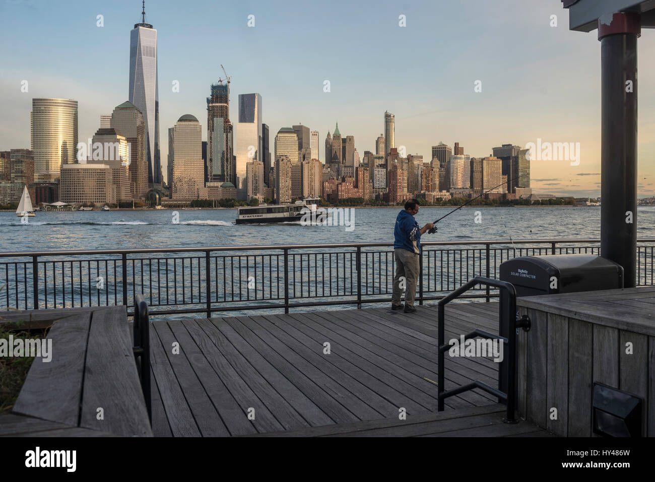 Jersey City, NJ, 26 Ottobre 2016 - pescatore in Jersey City lungomare con una vista della parte inferiore della Skyline di Manhattan con il World Trade Center e il viscosimetro Brookfield Plaza Foto Stock
