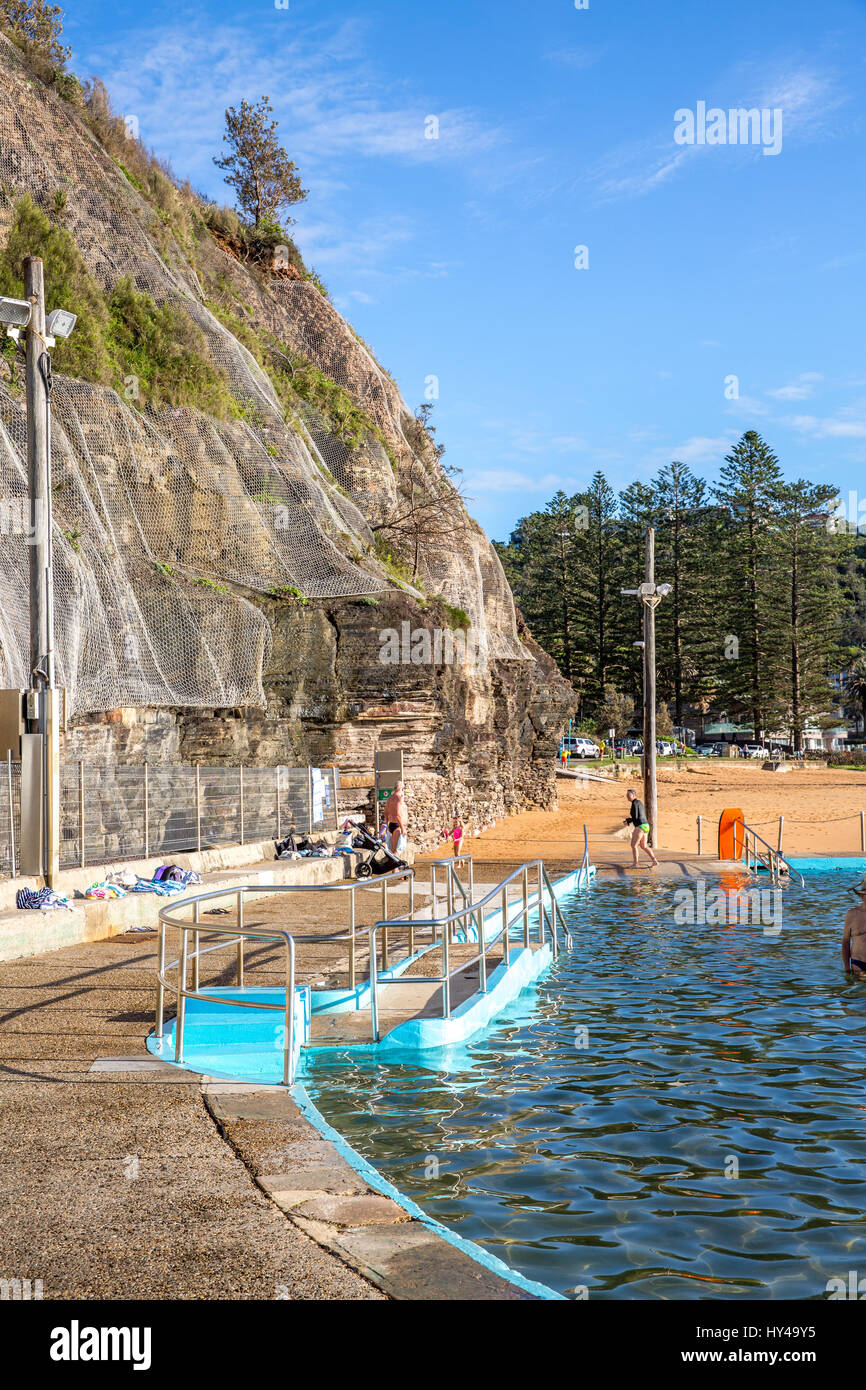 Le persone che si godono la mattina presto nuotare a Bilgola Beach Ocean rock pool a Sydney, Australia con rete di roccia per proteggere dalla caduta rocce scogliera Foto Stock