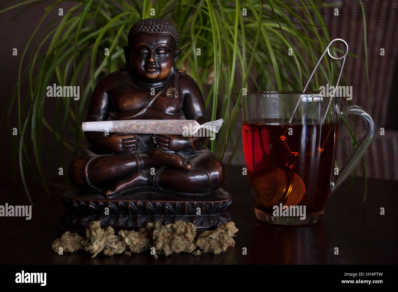 Primo piano della marijuana laminati giunto di erbaccia e gemme con la statuetta di Buddha e la tazza di tè rooibos sul terreno in legno Foto Stock