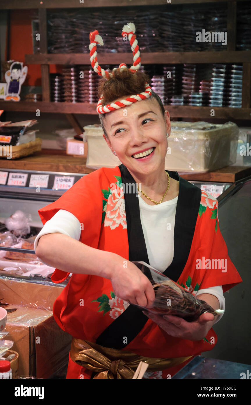 Donna Giapponese in costume tradizionale (una camicia happi) operando a una pressione di stallo di frutti di mare in un mercato. Il vecchio stile Giappone; mercato asiatico stallholder [cesdeh] Foto Stock