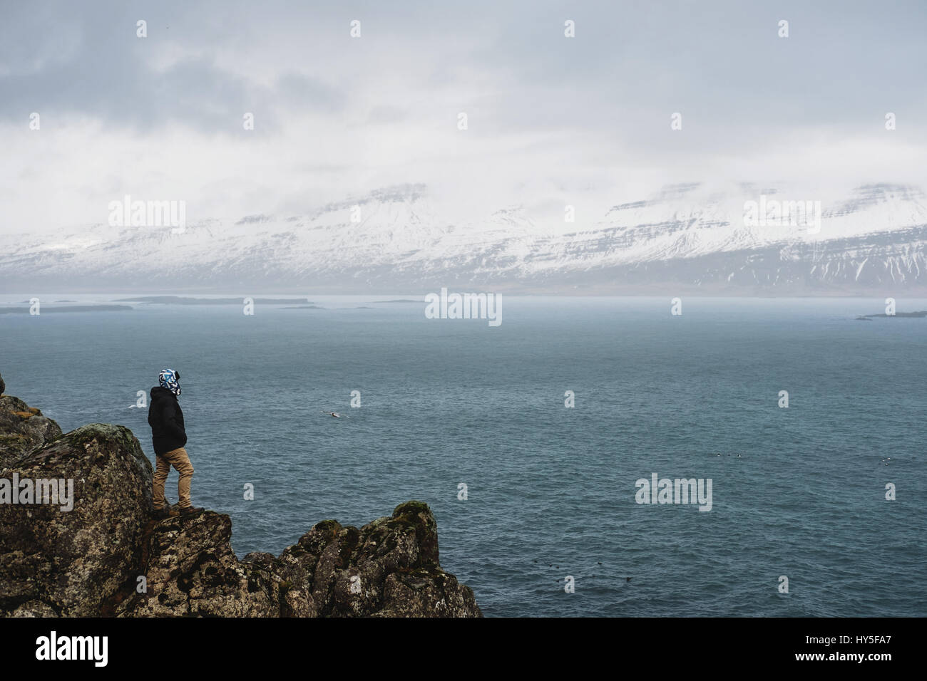 Un uomo in piedi sulla scogliera con l'oceano e la neve vista montagna Foto Stock