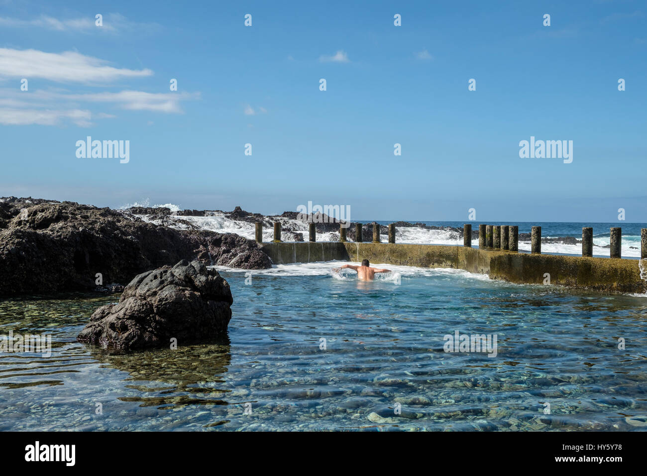 Un uomo gode di una rinfrescante nuotata nella ancora chiare acque blu di una roccia naturale piscina sulla costa di Tenerife vicino a Alcala mentre le onde dell'Atlantico o Foto Stock