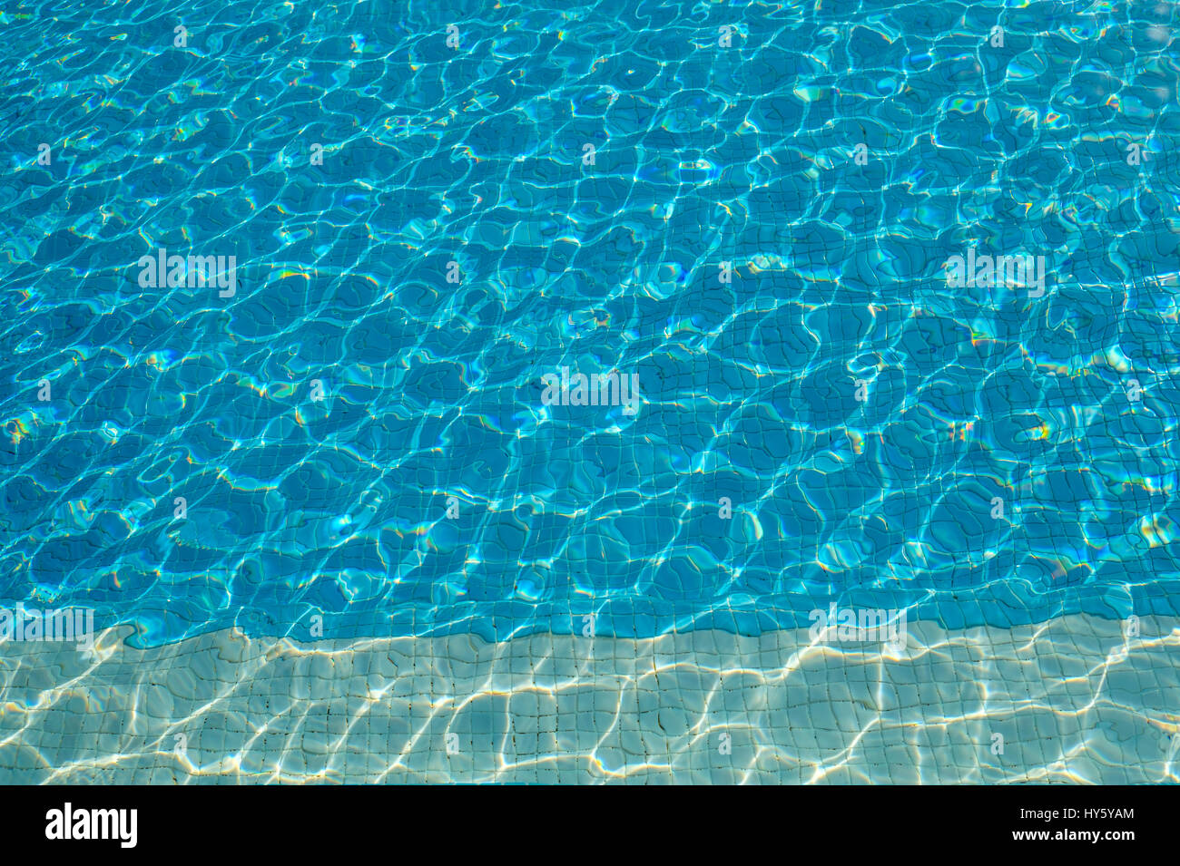 Sole che splende su un hotel piscina crea increspature e forme di luminoso blu turchese ideale per lo sfondo con spazio di copia Foto Stock