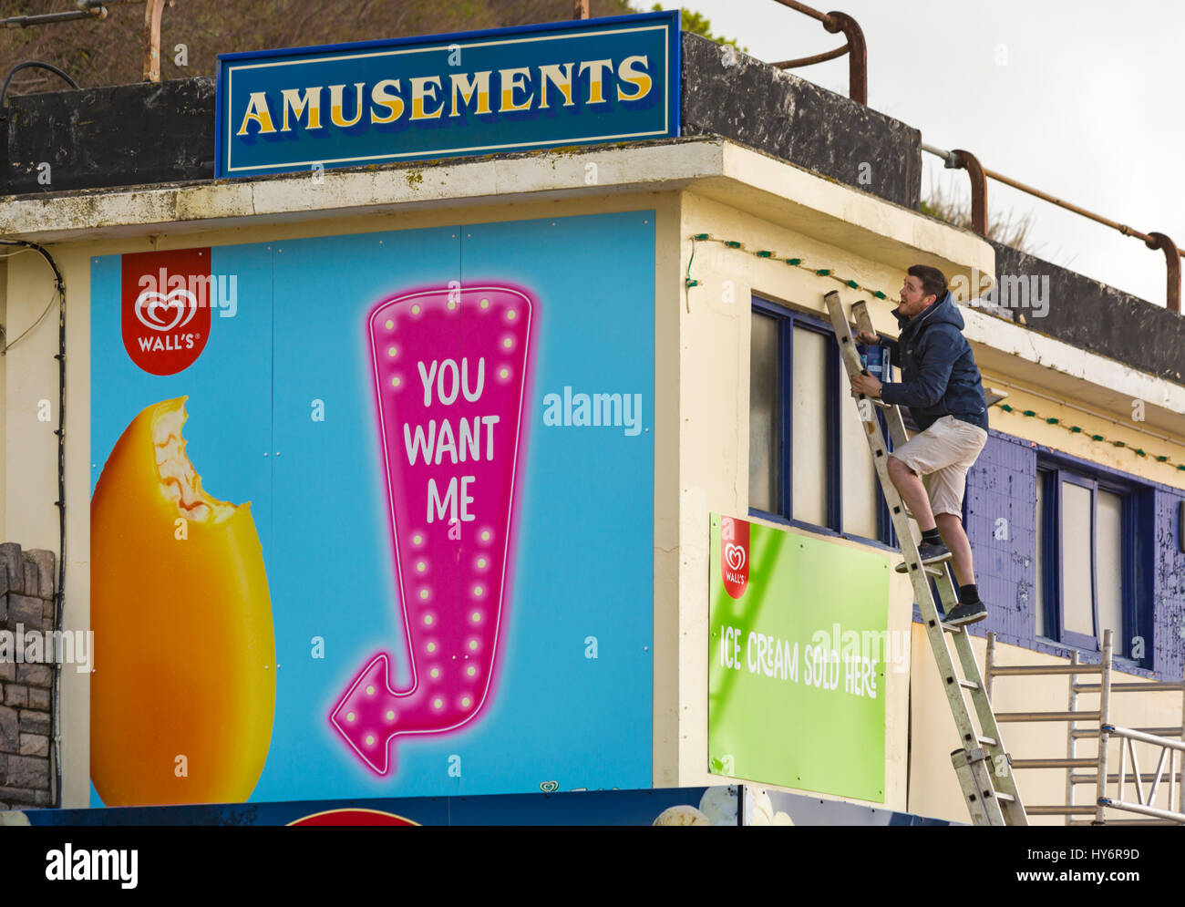 L'uomo scaletta con il vaso di vernice pittura divertimento arcade edificio sul lungomare di Bournemouth nel mese di aprile Foto Stock