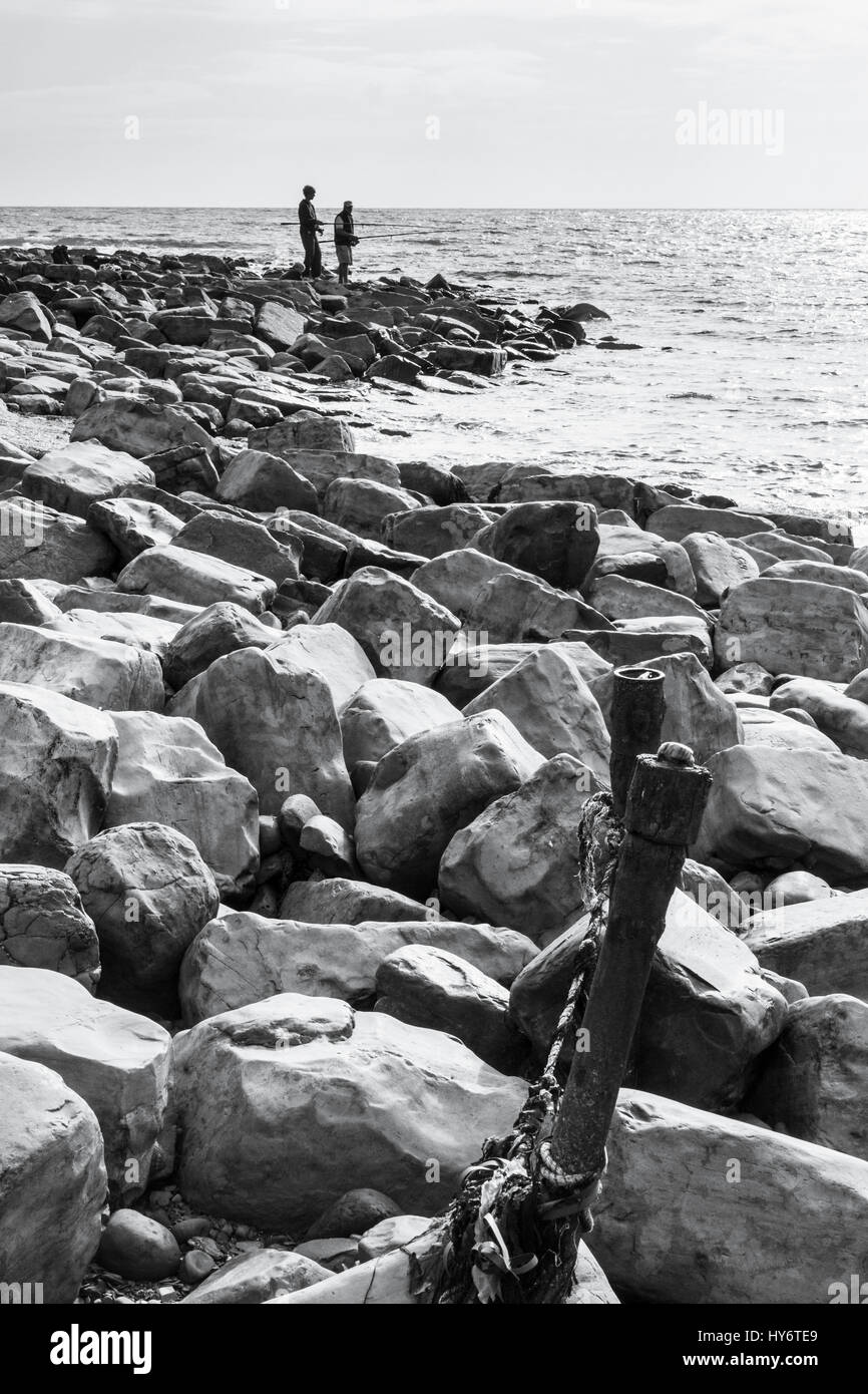 Immagine in bianco e nero di due pescatori di mare la pesca da un promontorio roccioso a Kimmeridge Bay, Dorset, England, Regno Unito Foto Stock