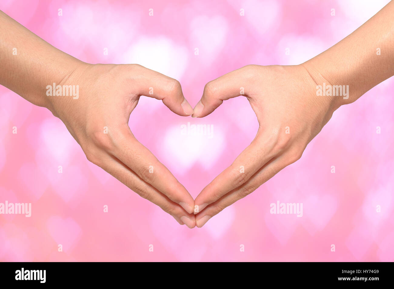 La forma del cuore fatto da mani maschio sul cuore rosa sfondo bokeh di fondo Foto Stock