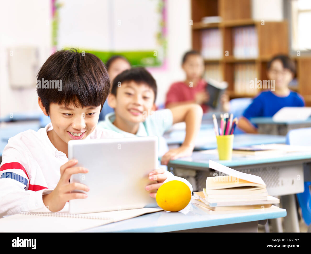Asian scuola elementare bambino utilizzando computer tablet in aula, felice e sorridente. Foto Stock