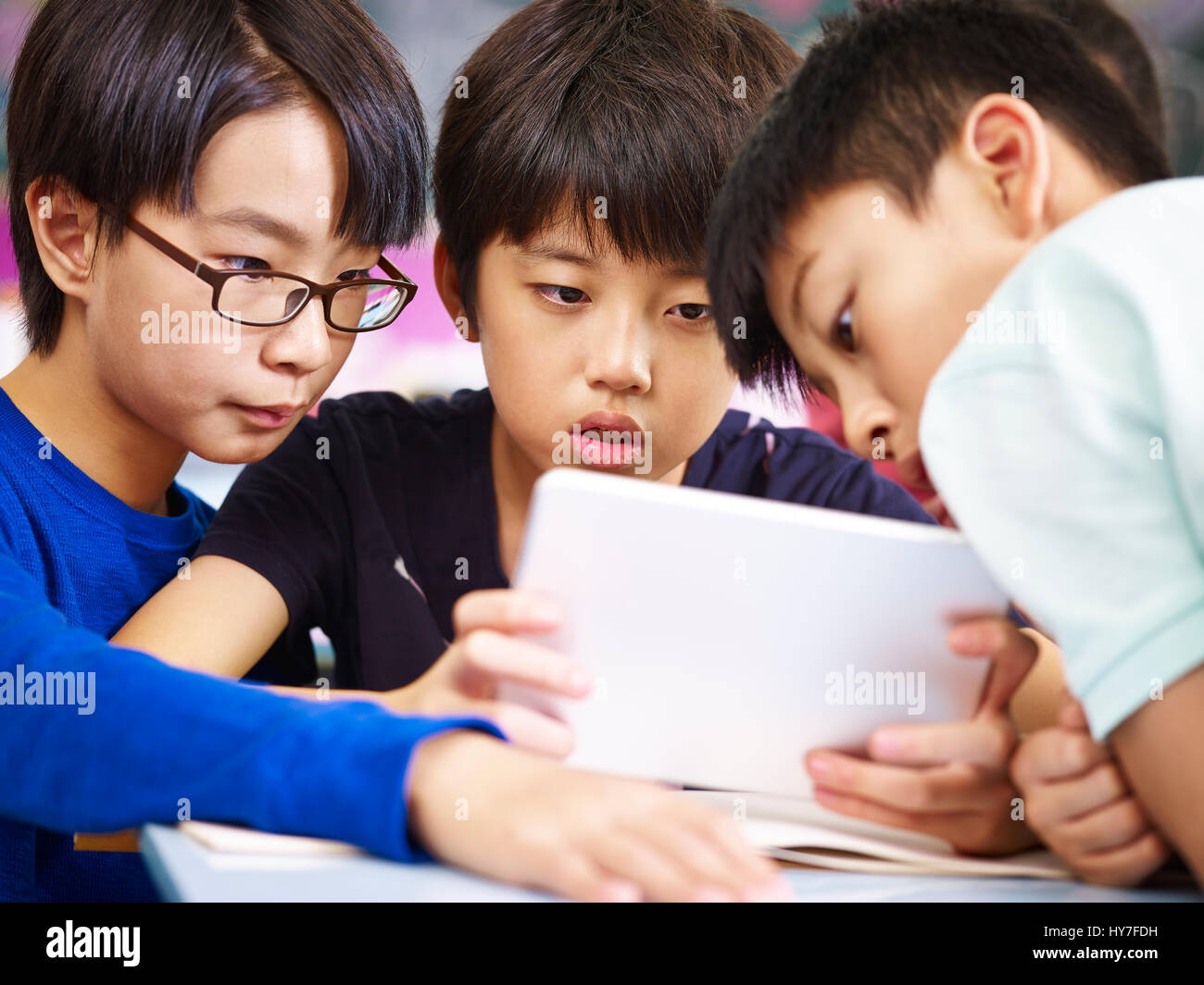 Tre asiatici scuola primaria studente la riproduzione del video gioco utilizzando computer tablet con gravi l'espressione del viso. Foto Stock