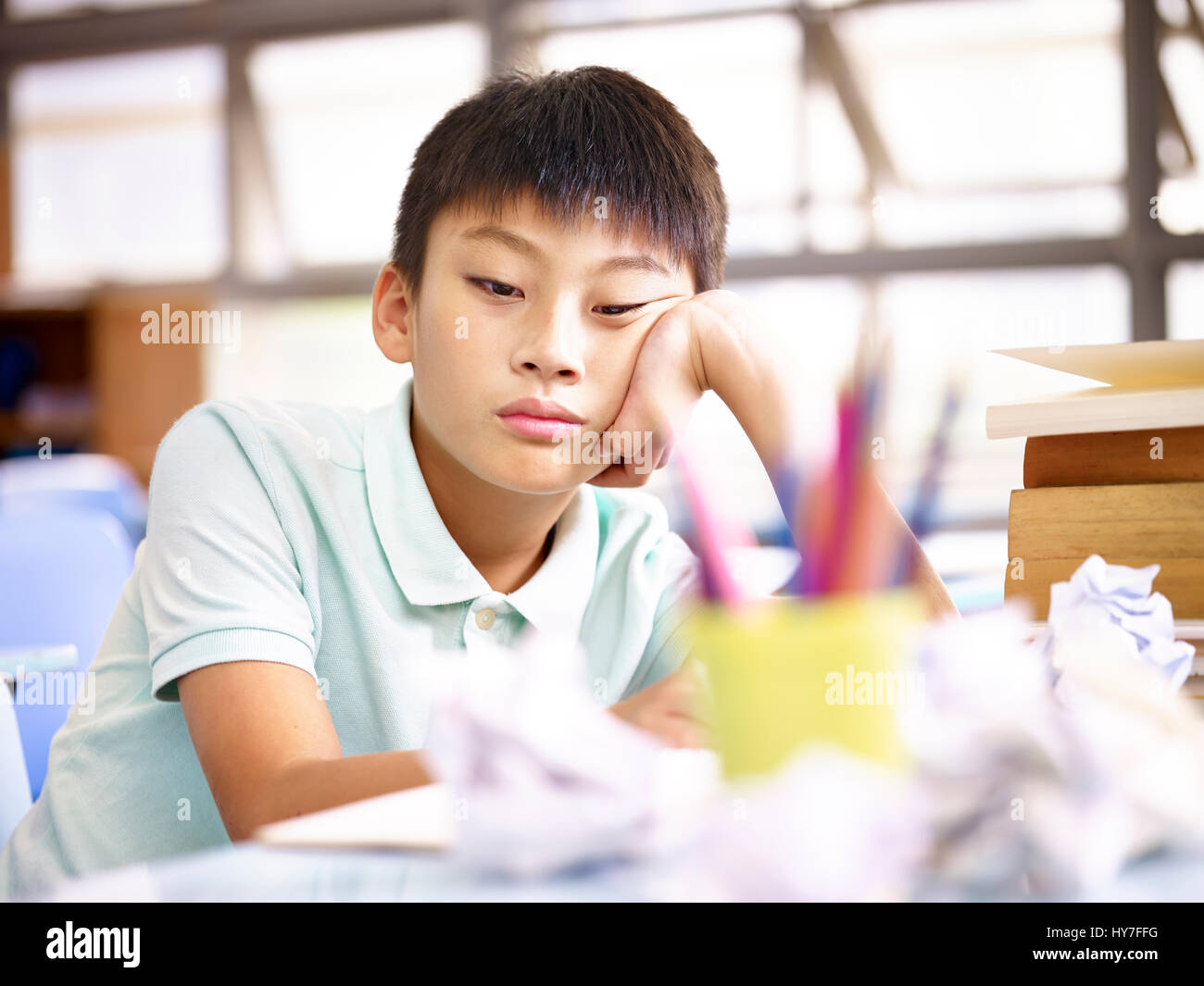 Triste e frustrato scuola asiatica ragazzo seduto da solo in aula con la carta sbriciolato sulla scrivania. Foto Stock