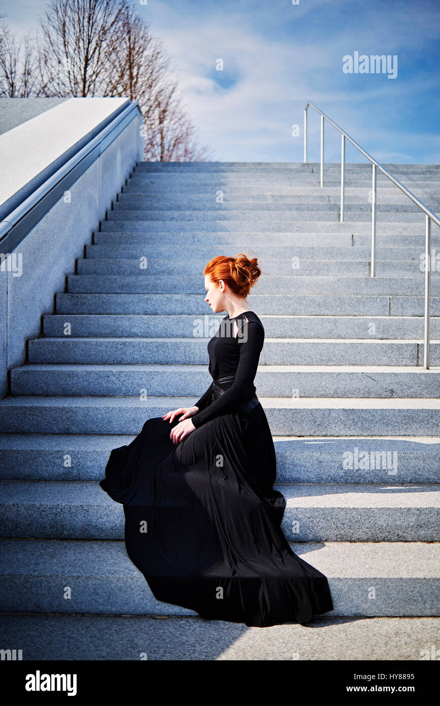 La donna elegante con i capelli rossi seduto sui gradini in abito nero di New York City Foto Stock