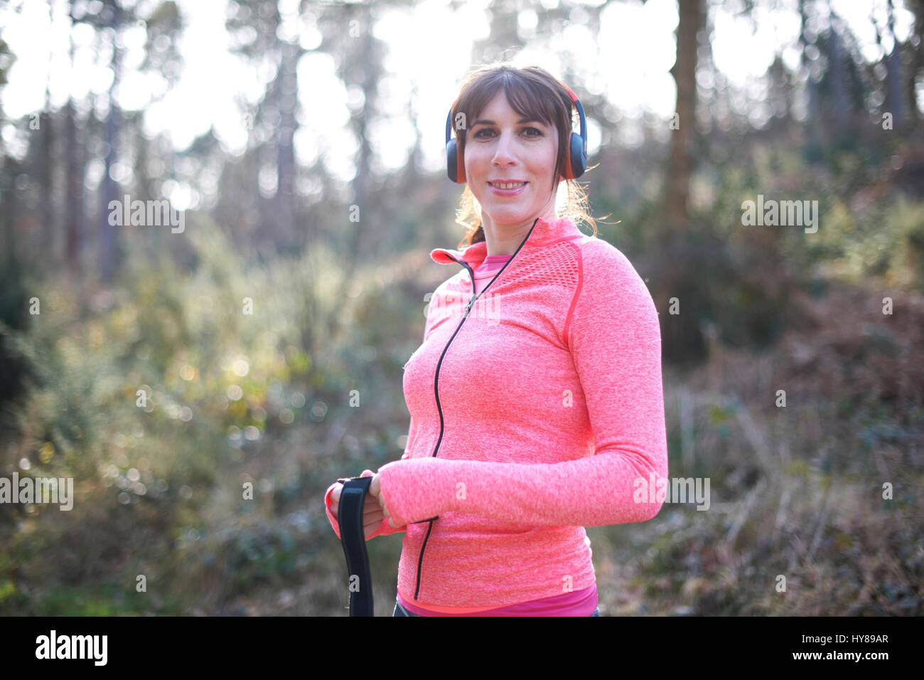 Una giovane donna che indossa le cuffie durante l'esercizio nei boschi Foto Stock