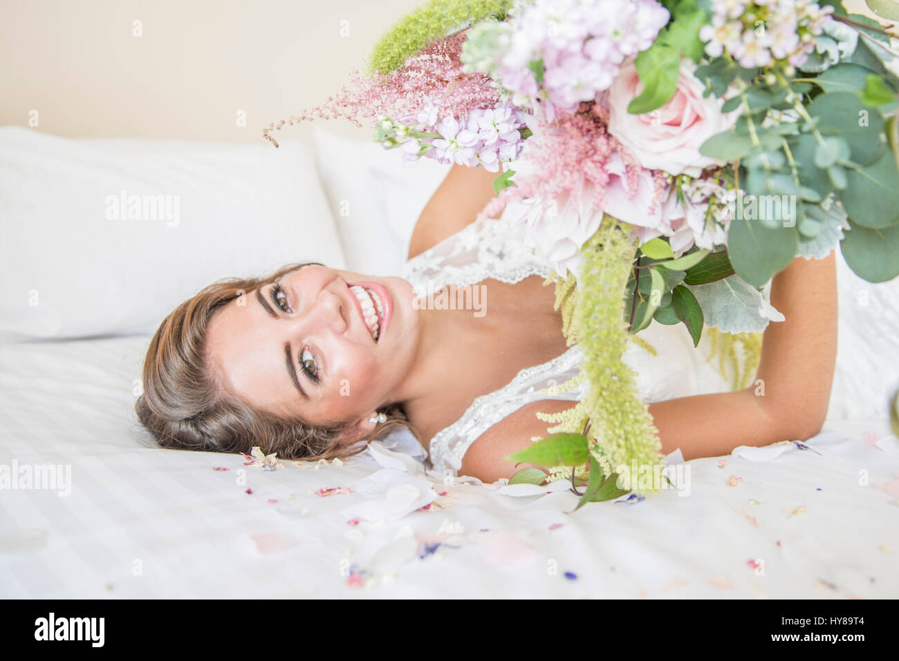 Una sposa la posa sul letto nella sua suite nuziale mentre tiene un mazzo di fiori Foto Stock