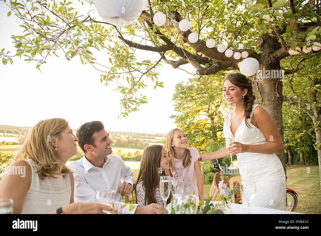 La sposa e lo sposo seduti al tavolo in alto con i loro amici a un matrimonio esterno Foto Stock