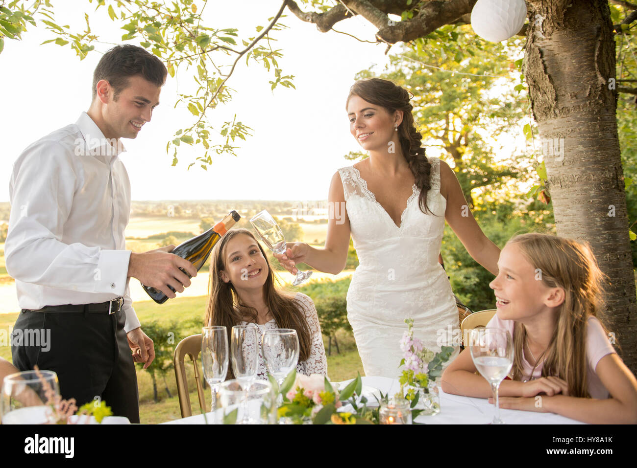 La sposa e lo sposo seduti al tavolo in alto con i loro amici a un matrimonio esterno Foto Stock