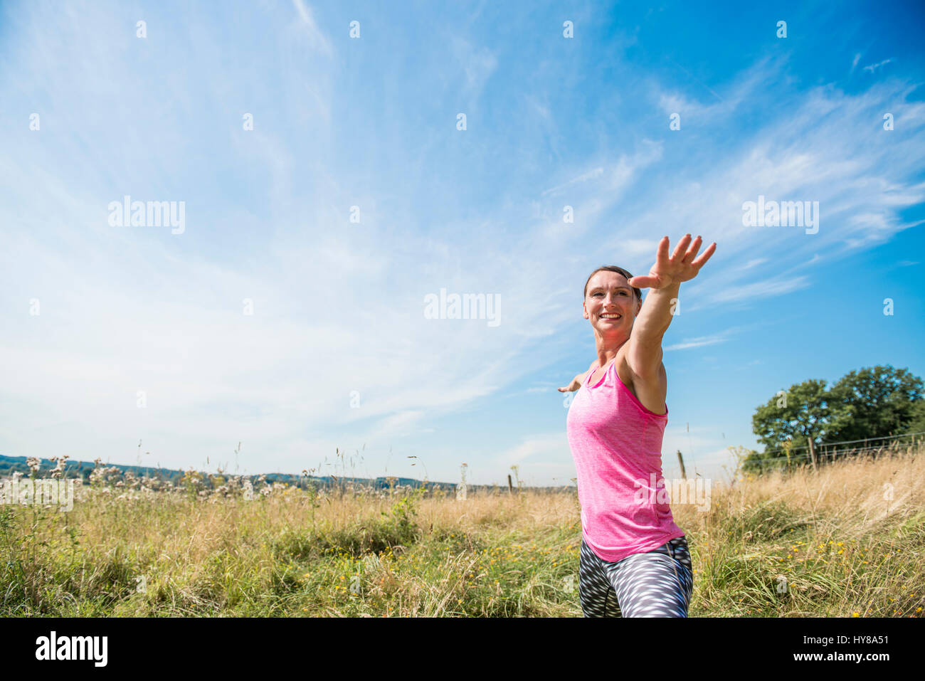 Una donna gode di una posizione soleggiata giornata fuori in un prato mentre la pratica dello yoga Foto Stock
