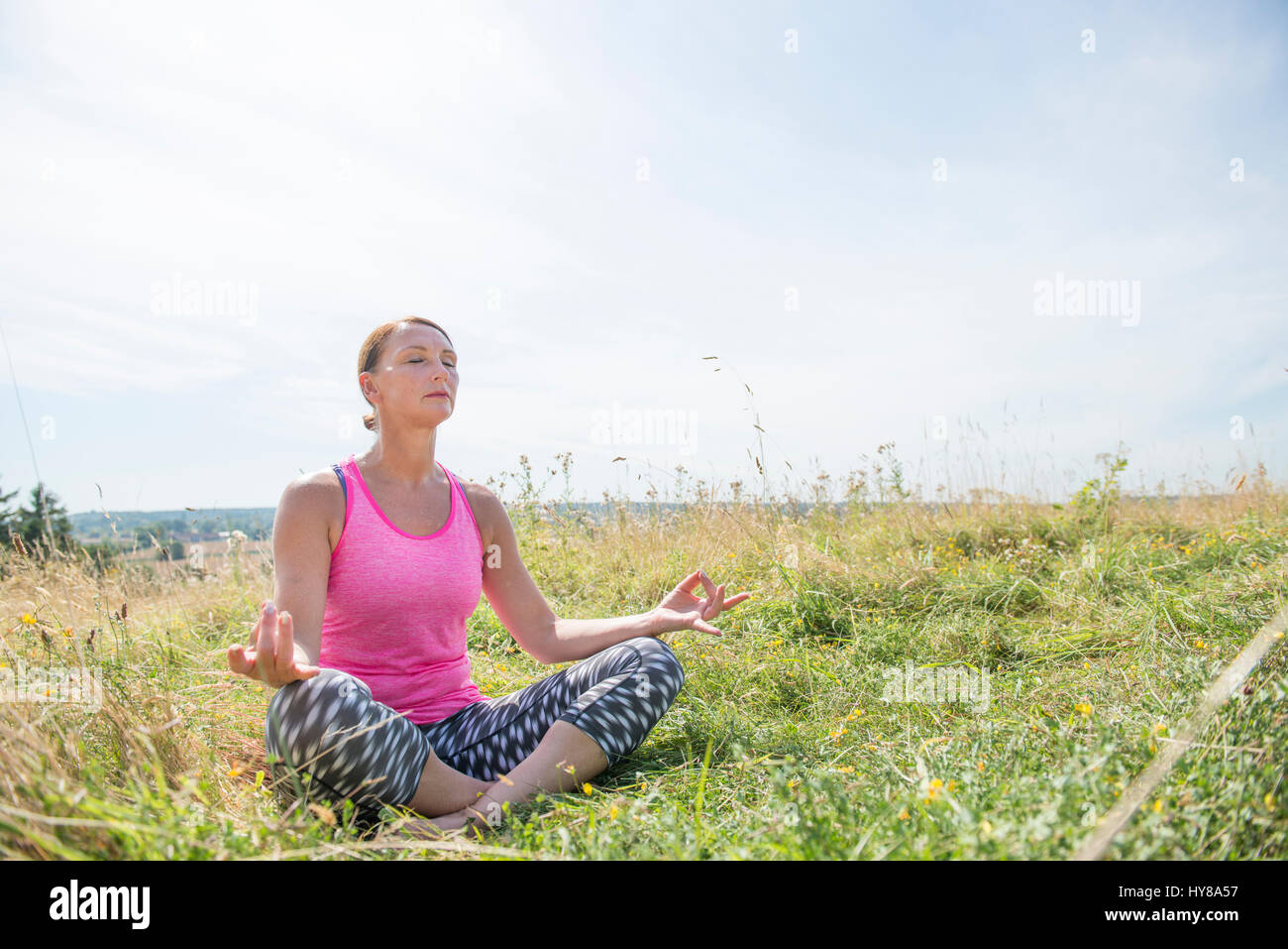 Una donna gode di una posizione soleggiata giornata fuori in un prato mentre la pratica dello yoga Foto Stock