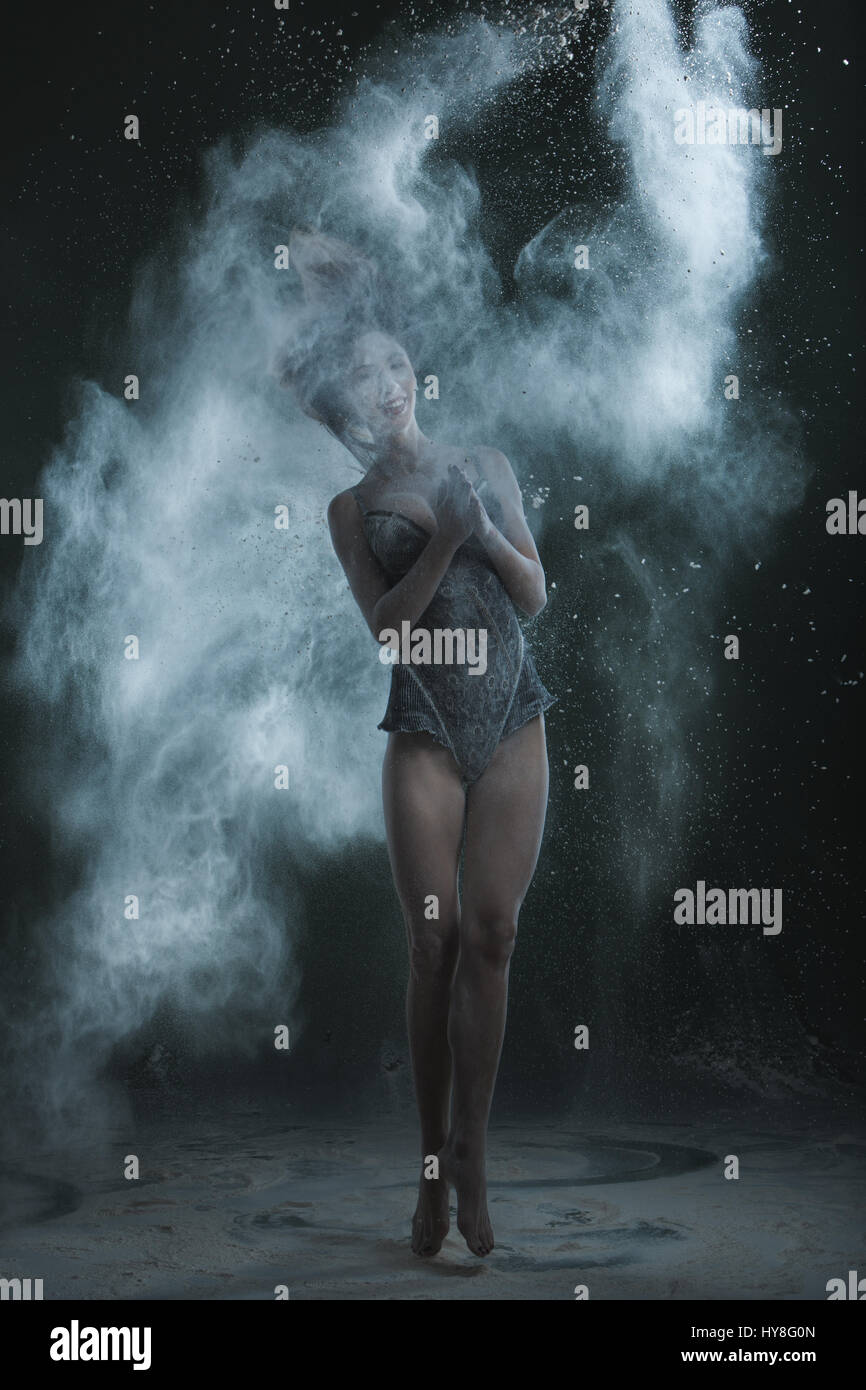Donna danze in polvere di farina. Donna balli in una nuvola di polvere di farina su uno sfondo nero. Foto Stock