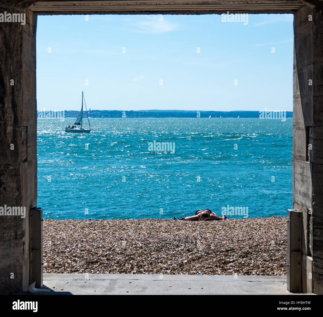 Una vista attraverso la porta di Sally nella vecchia Portsmouth con una donna a prendere il sole sulla spiaggia mentre uno yacht di vele da Foto Stock