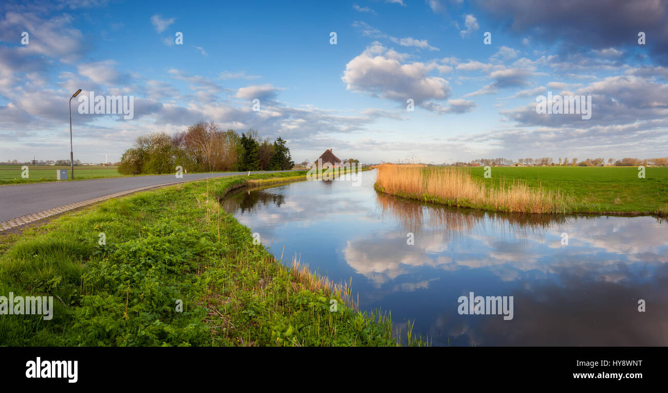 Il cielo blu con nuvole riflettono in acqua, su strada, case vicino al canal, alberi, erba verde e giallo ance a sunrise in Paesi Bassi. Incredibile colorato Foto Stock