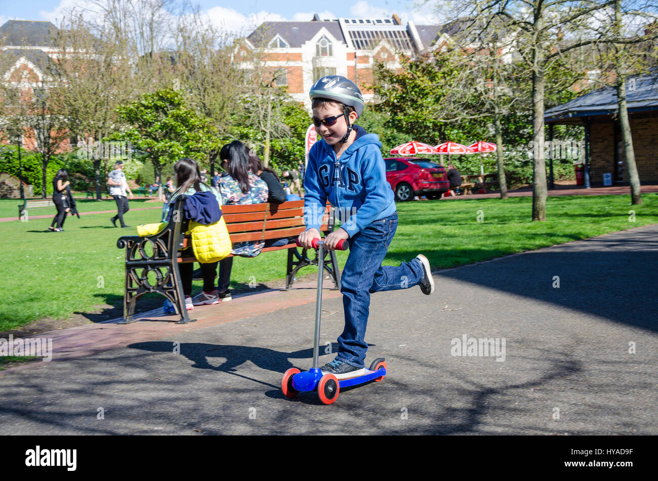 Un giovane ragazzo in sella a un scooter push nel parco. Foto Stock