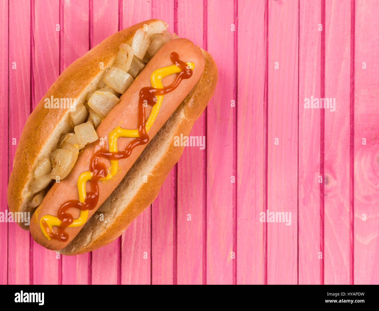 Hot Dog in un panino con cipolle fritte ketchup e senape contro un sfondo rosa Foto Stock